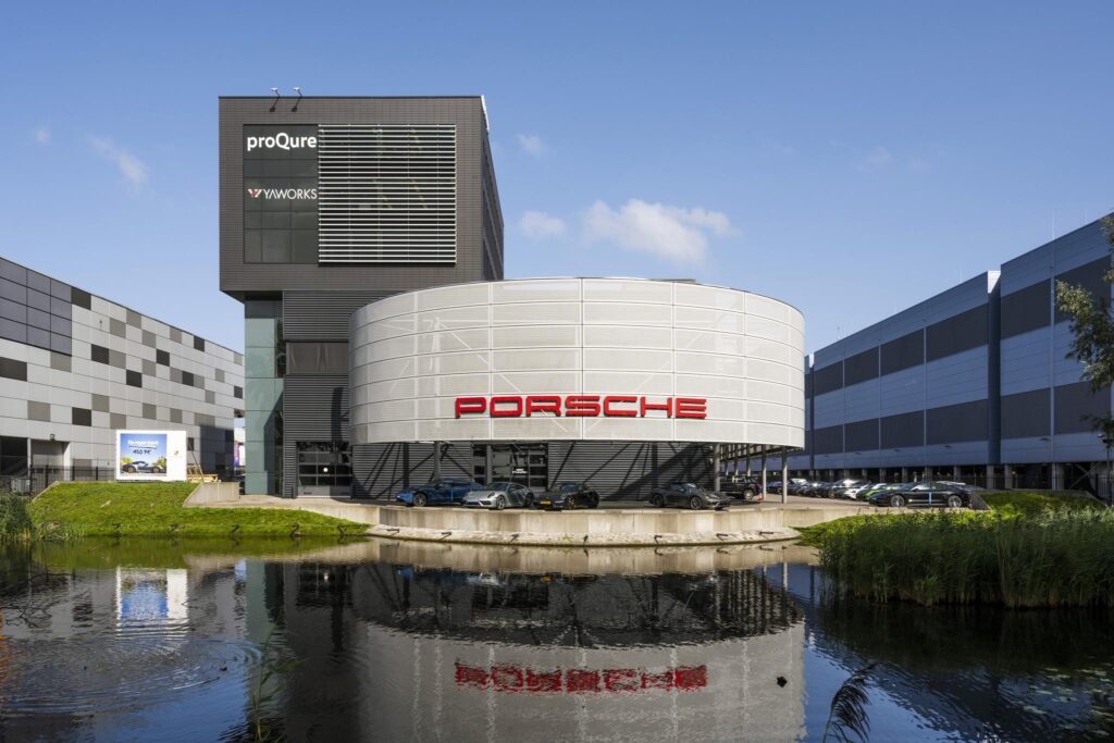 Modern kantoorgebouw aan de Sijsjesbergweg met opvallende Porsche-showroom en spiegeling in het water.