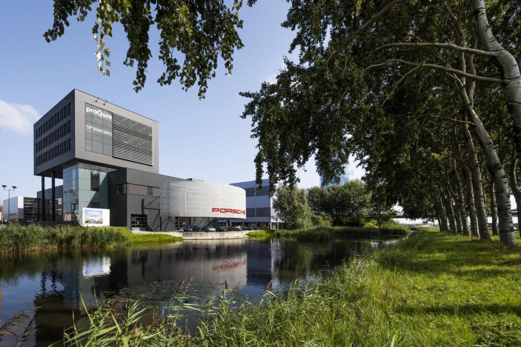 Modern bedrijfsgebouw met Porsche-showroom aan de Sijsjesbergweg, gelegen naast een groene waterpartij met bomen.