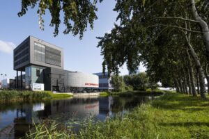Modern bedrijfsgebouw met Porsche-showroom aan de Sijsjesbergweg, gelegen naast een groene waterpartij met bomen.