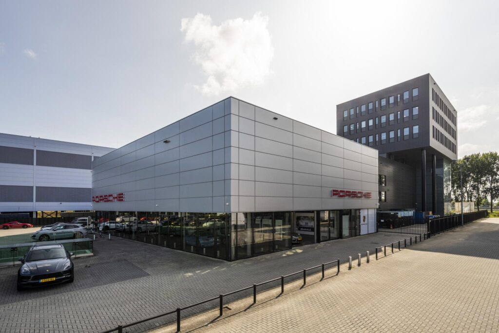 Voorgevel van het Porsche Centrum aan de Sijsjesbergweg met moderne architectuur en geparkeerde sportwagens.