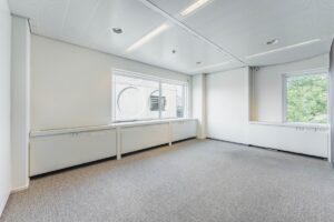 Licht, leeg kantoor aan de Laarderhoogtweg met grote ramen en grijze vloerbedekking.