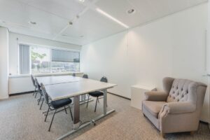 Vergaderruimte aan de Laarderhoogtweg met een vergadertafel, zes stoelen en een comfortabele fauteuil bij het raam.