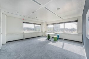 Lichte kantoorruimte aan de Laarderhoogtweg met grote ramen, uitzicht op omliggende kantoorgebouwen en minimalistische inrichting met enkele zitmeubels.