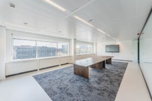 Moderne vergaderruimte aan de Laarderhoogtweg met een lange houten tafel, groot scherm en uitzicht op kantoorgebouwen.