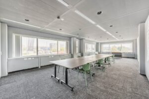 Moderne vergaderruimte aan de Laarderhoogtweg met grote ramen, vergadertafels en groene stoelen.