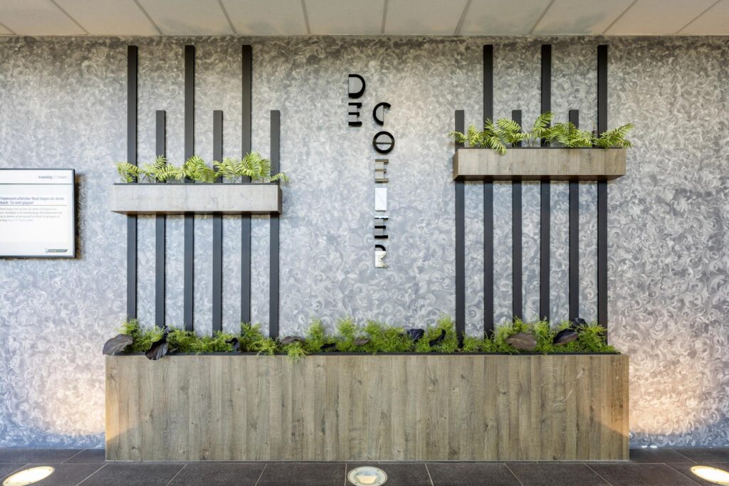 Modern interior wall with vertical black bars, decorative planters, and "De Coender" signage at Overschiestraat.