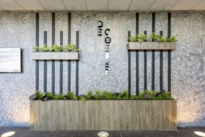 Modern interior wall with vertical black bars, decorative planters, and "De Coender" signage at Overschiestraat.