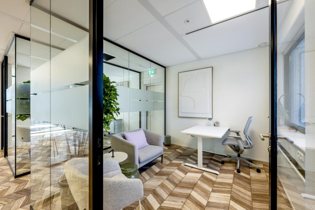 Modern glass-walled office at Overschiestraat with a desk, ergonomic chair, and seating area.