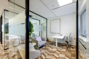 Modern glass-walled office at Overschiestraat with a desk, ergonomic chair, and seating area.