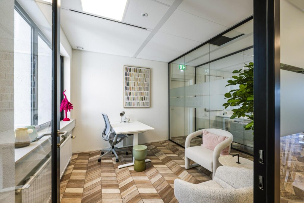 Modern office space on Overschiestraat with a desk, ergonomic chair, glass walls, and cozy seating area.