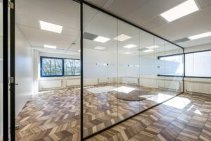 Modern office space on Overschiestraat with glass walls, patterned wooden flooring, and large windows.