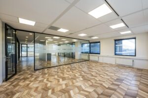 Modern office space on Overschiestraat with glass walls, patterned wooden floor tiles, and large windows.