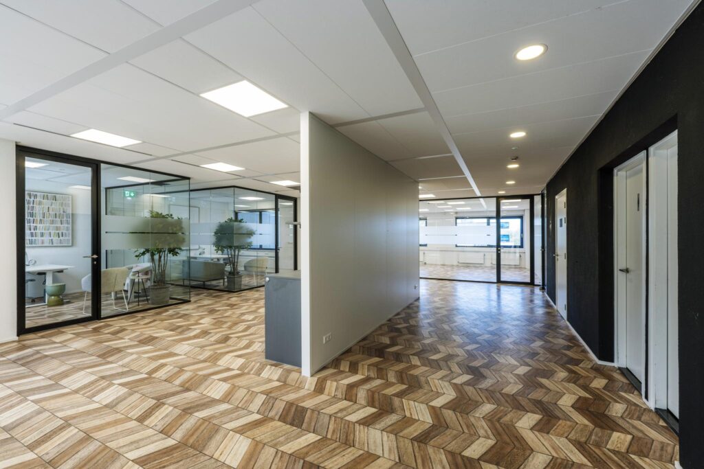 Modern office hallway on Overschiestraat with glass meeting rooms and patterned wooden flooring.
