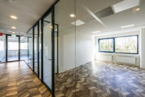 Modern office space on Overschiestraat with glass walls, patterned wooden flooring, and large windows.