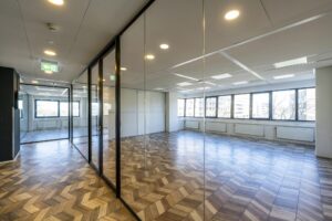 Modern empty office space at Overschiestraat with large windows, glass walls, and patterned wooden flooring.