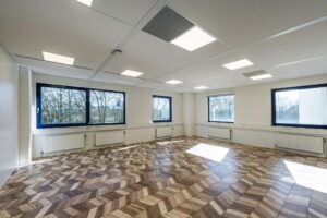 Bright, empty office space on Overschiestraat with large windows and a patterned wooden floor.