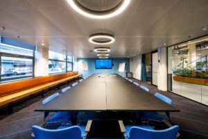 Moderne vergaderruimte aan de Kabelweg met lange conferentietafel, blauwe stoelen, presentatievoorzieningen en grote ramen.