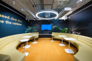 Moderne vergaderruimte met ronde gele bank, witte tafels, planten en een scherm aan de muur bij Kabelweg.
