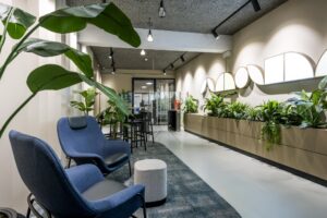 Moderne wachtruimte met blauwe loungefauteuils, veel planten en kunstzinnige wandverlichting in een kantoor aan de Singel.