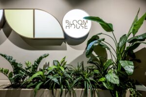 Wanddecoratie met het verlichte logo van Bloom House boven een plantenbak met diverse tropische kamerplanten.