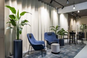 Moderne wachtruimte met blauwe loungefauteuils, hoge planten en een stijlvolle lichtinval tegen een geribbelde wand.