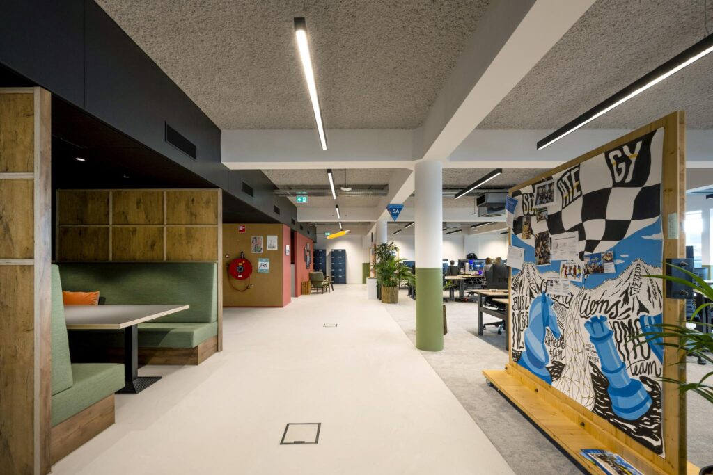 Moderne kantoorruimte met flexibele werkplekken, een zithoek en een kleurrijk beschilderd prikbord.