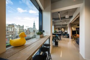 Modern kantoorinterieur aan het Singel in Amsterdam met uitzicht op de stad en een gele badeend op de vensterbank.