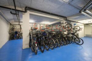Fietsenstalling met dubbelzijdig fietsrek in een kelderruimte met blauwe vloer.