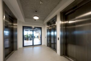 Hal met drie gesloten liften en een glazen schuifdeur naar een kantoorruimte op Singel 174.