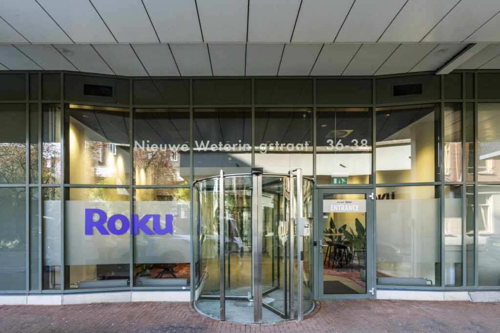Entrance of the Roku office at Nieuwe Weteringstraat 36–38 with a glass revolving door and signage.