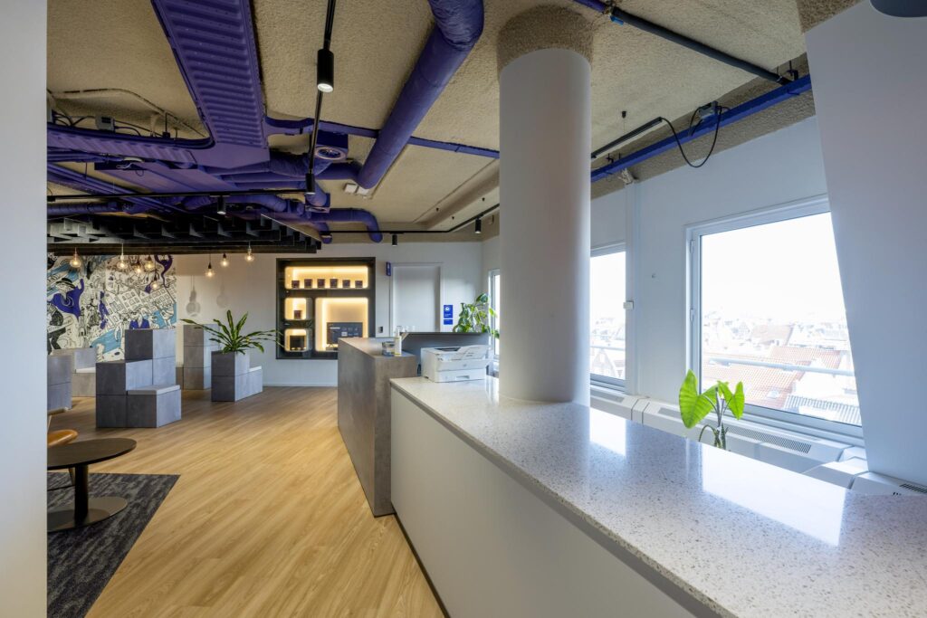 Modern office interior on the Vijzelgracht with purple ceiling pipes, a reception desk, lounge seating, and large windows with city views.