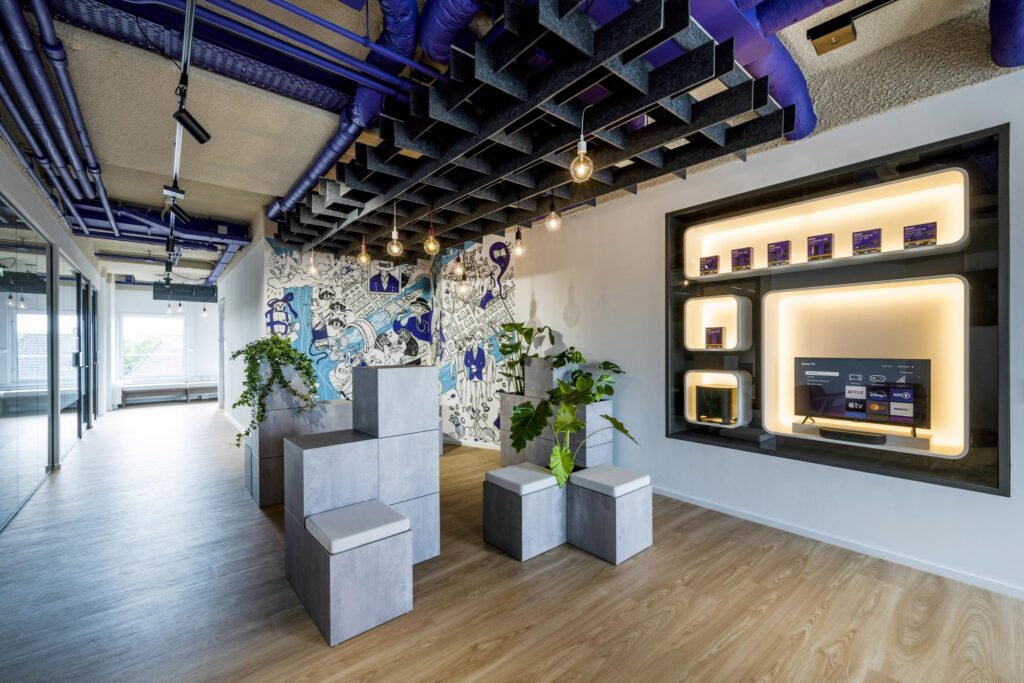 Modern office interior with colorful wall art, geometric seating blocks, and a built-in display featuring digital streaming services.