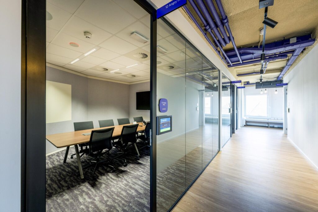 Modern glass-walled meeting room named "12 Angry Men" with a long table and office chairs, located in a bright corridor at Vijzelgracht.