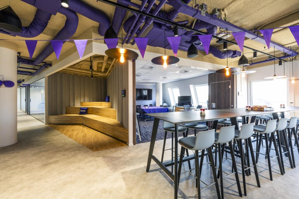 Modern office space on Vijzelgracht with high tables, a wooden seating area, and purple ceiling decorations.