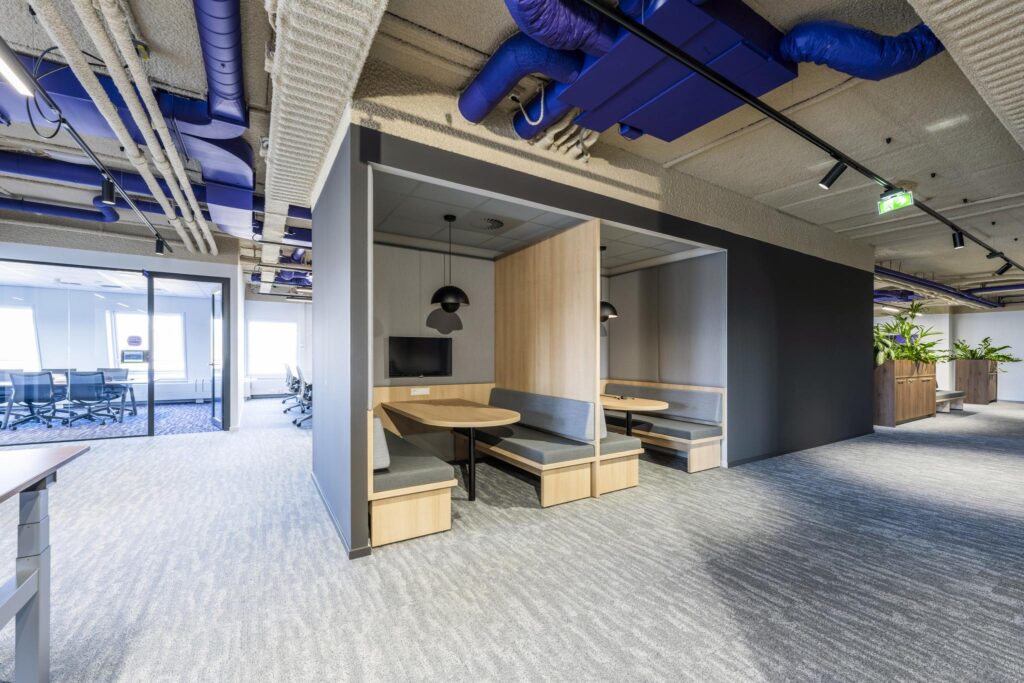 Modern office interior with built-in meeting booths, a visible ceiling with blue ductwork, and a glass-walled conference room.