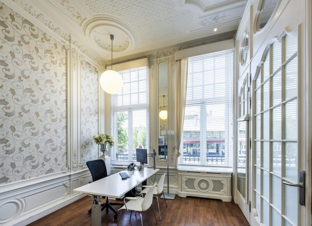 Elegant office space with classic ornate interior, large windows, and a modern desk setup overlooking Concertgebouwplein.