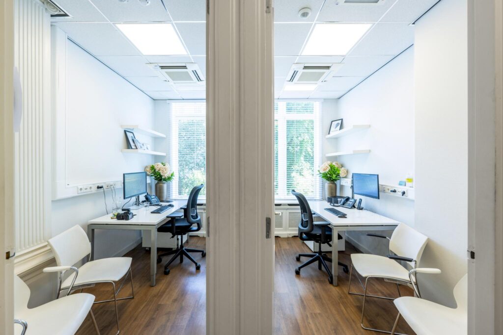 Two bright, modern office rooms with desks, chairs, and large windows overlooking greenery at Concertgebouwplein.