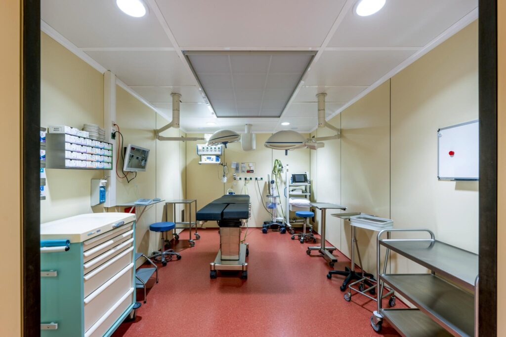 Modern medical examination room with an operating table, equipment, and surgical lighting.