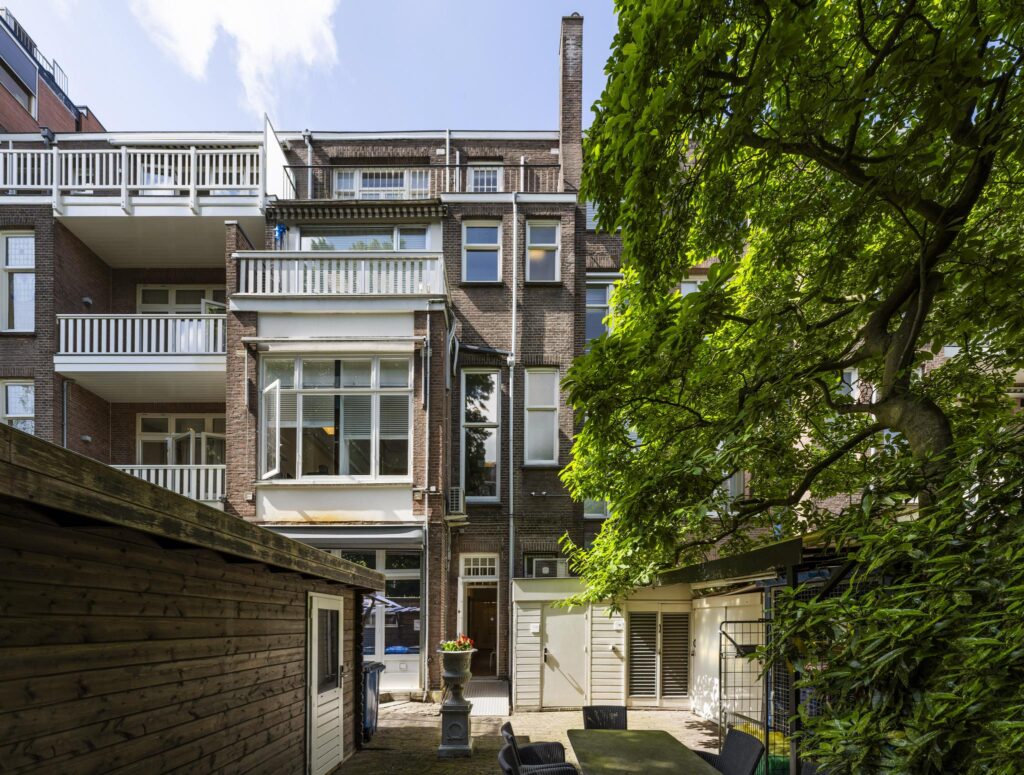 Rear view of a traditional Amsterdam apartment building on Concertgebouwplein with balconies, a garden, and green tree canopy.