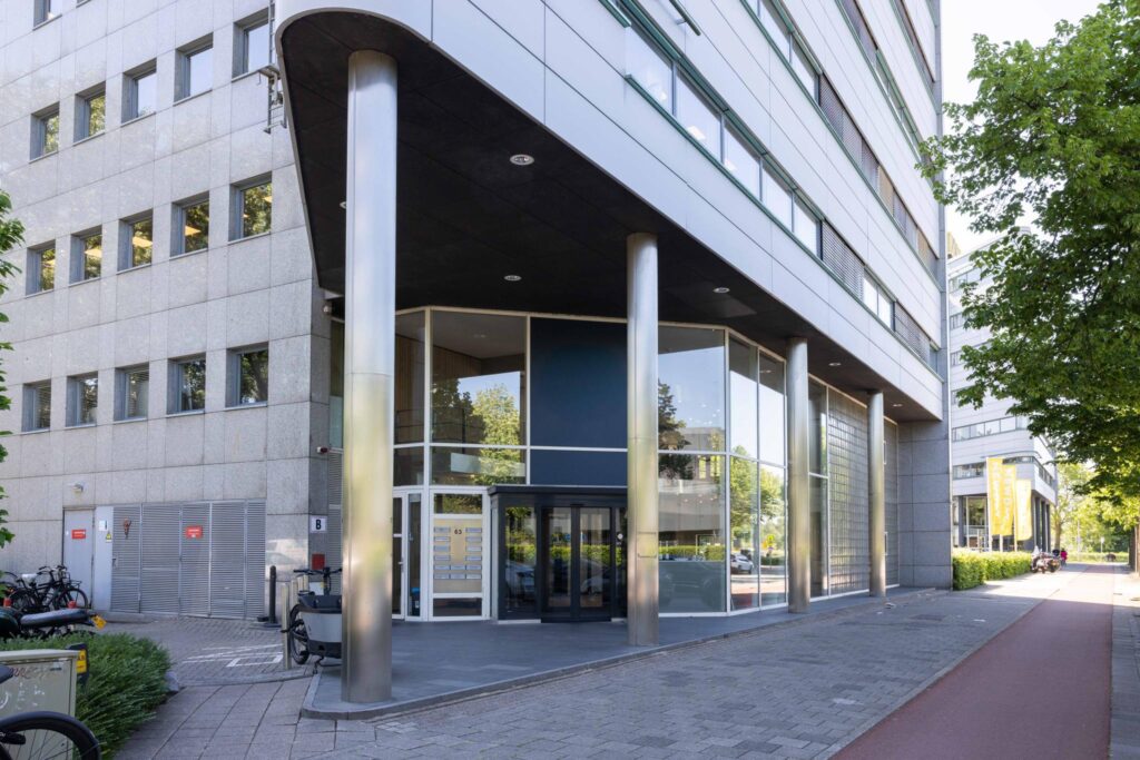Entrance of a modern office building on Overschiestraat in Amsterdam with large glass windows and metal columns.