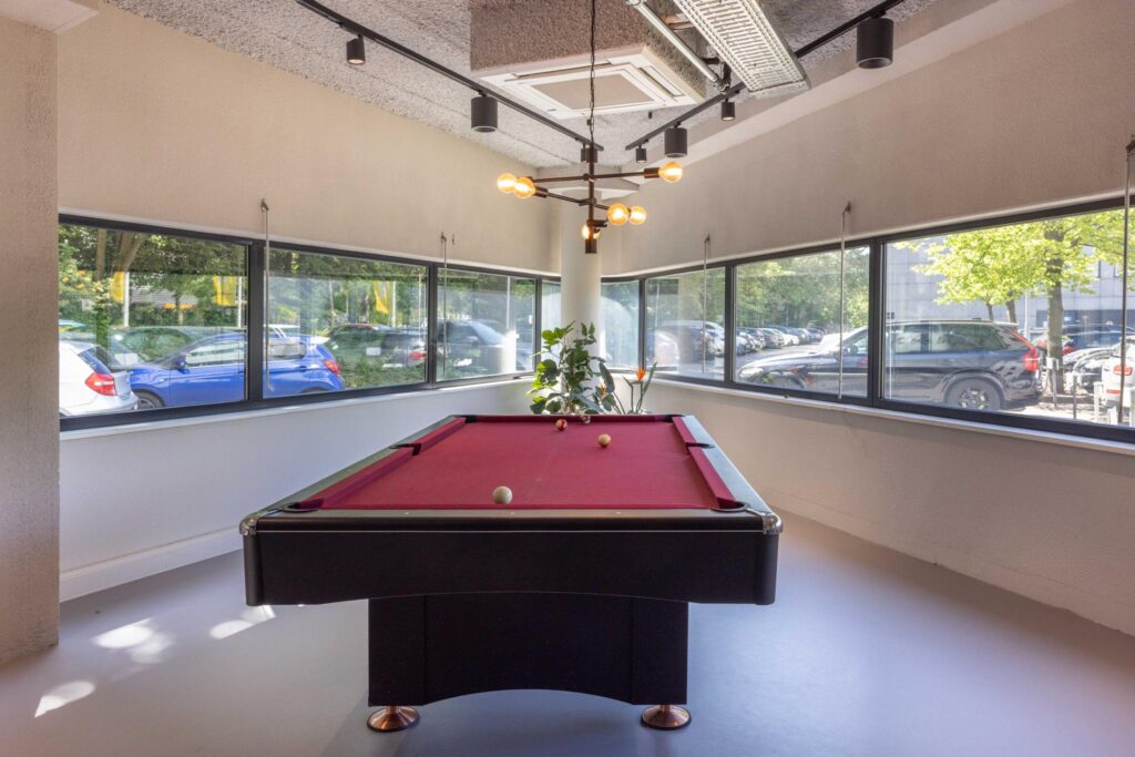 Modern recreation room with a red pool table near large windows at Overschiestraat.