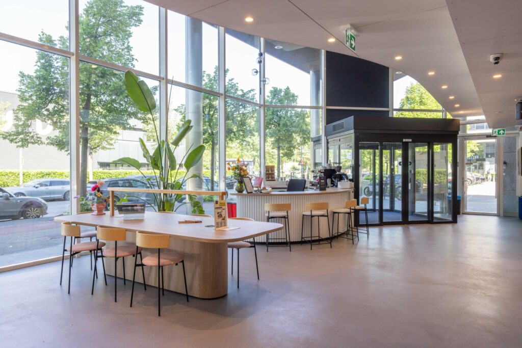 Modern lobby with large windows, a wooden communal table, and a coffee bar at Overschiestraat 235.