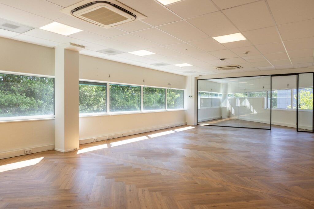 Bright and spacious office space on Overschiestraat with large windows, glass partition walls, and wooden herringbone flooring.