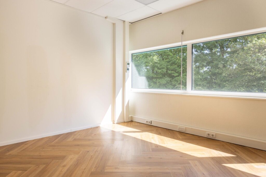 Bright, empty office space with herringbone wooden flooring and large windows overlooking greenery on Overschiestraat.