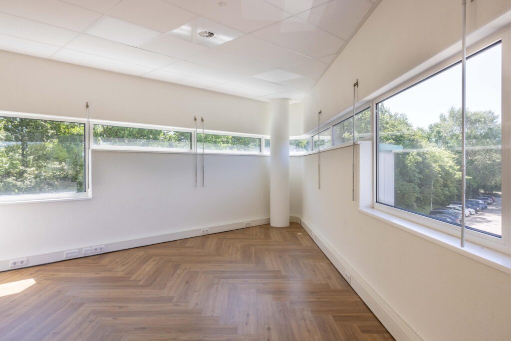 Bright empty office space on Overschiestraat with large windows and herringbone wooden flooring.