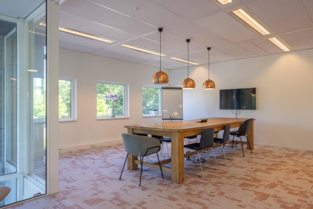 Modern meeting room at Overschiestraat with a wooden table, pendant lights, and large windows.
