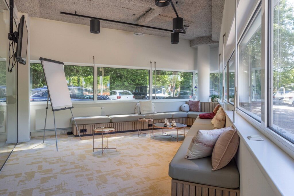 Modern lounge-style meeting room at Overschiestraat with large windows, cushioned bench seating, and a flipchart.
