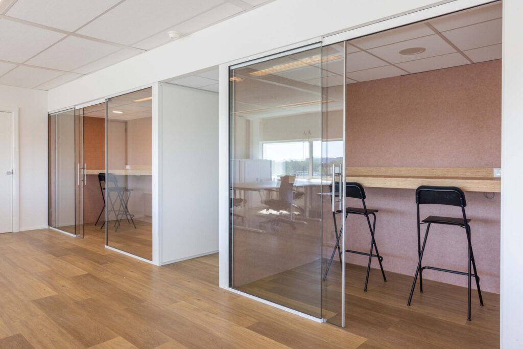 Modern office space on Overschiestraat with glass-walled work booths and high chairs.