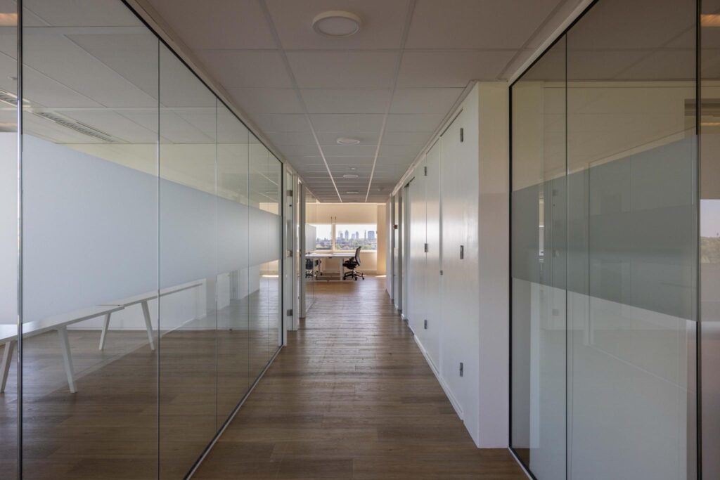 Modern office hallway with glass walls and a view of the city skyline in the distance.