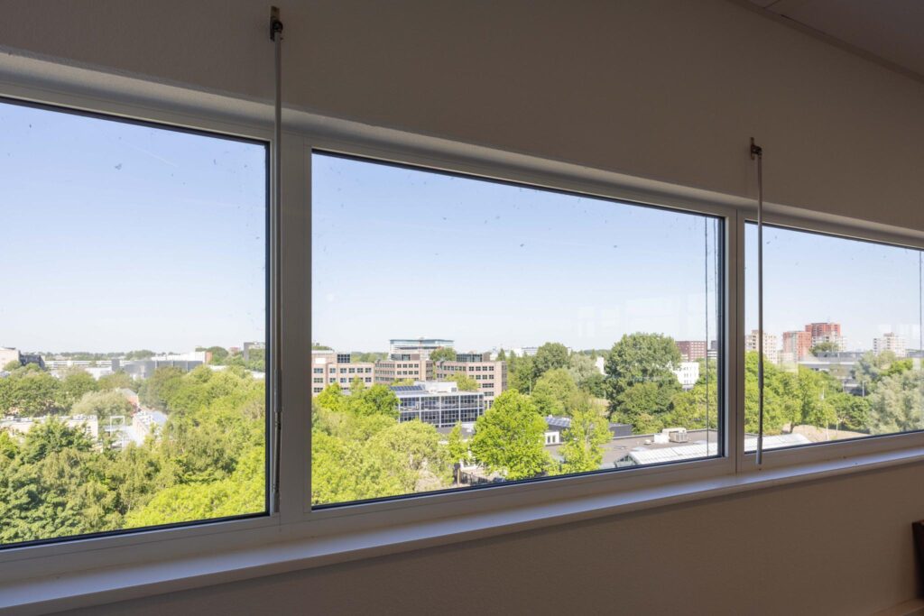 View from a high window overlooking green trees and office buildings on Overschiestraat.